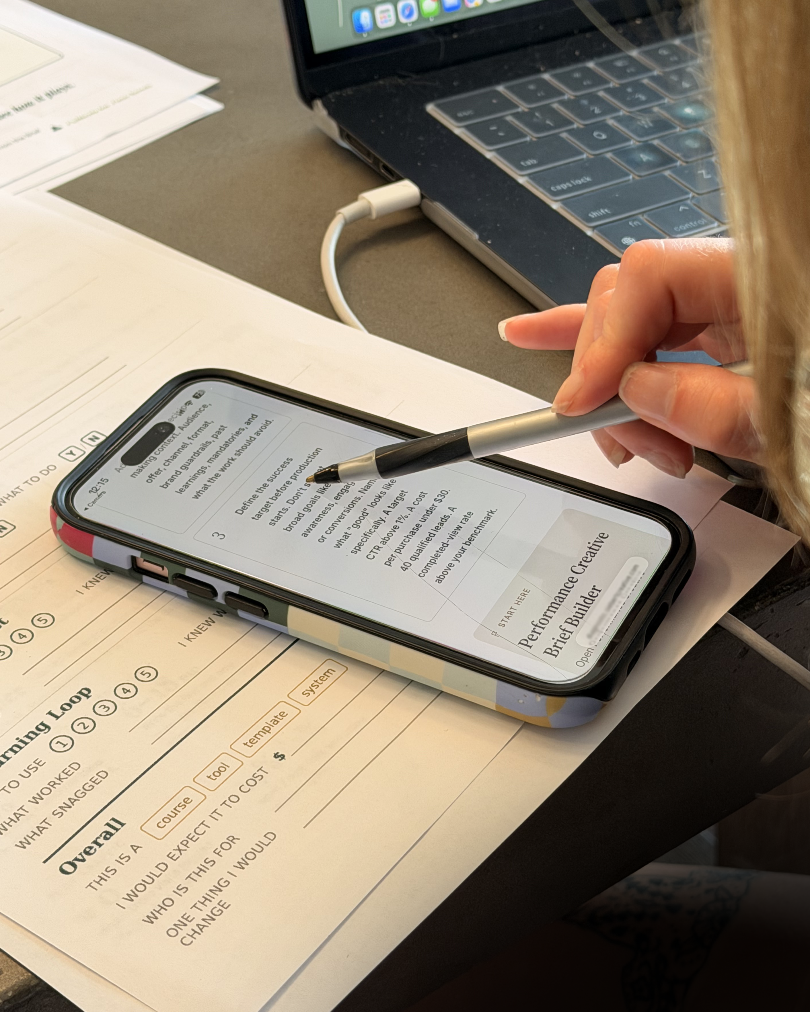 Hand with stylus on the Brief Builder, printed capture sheets on a warm table